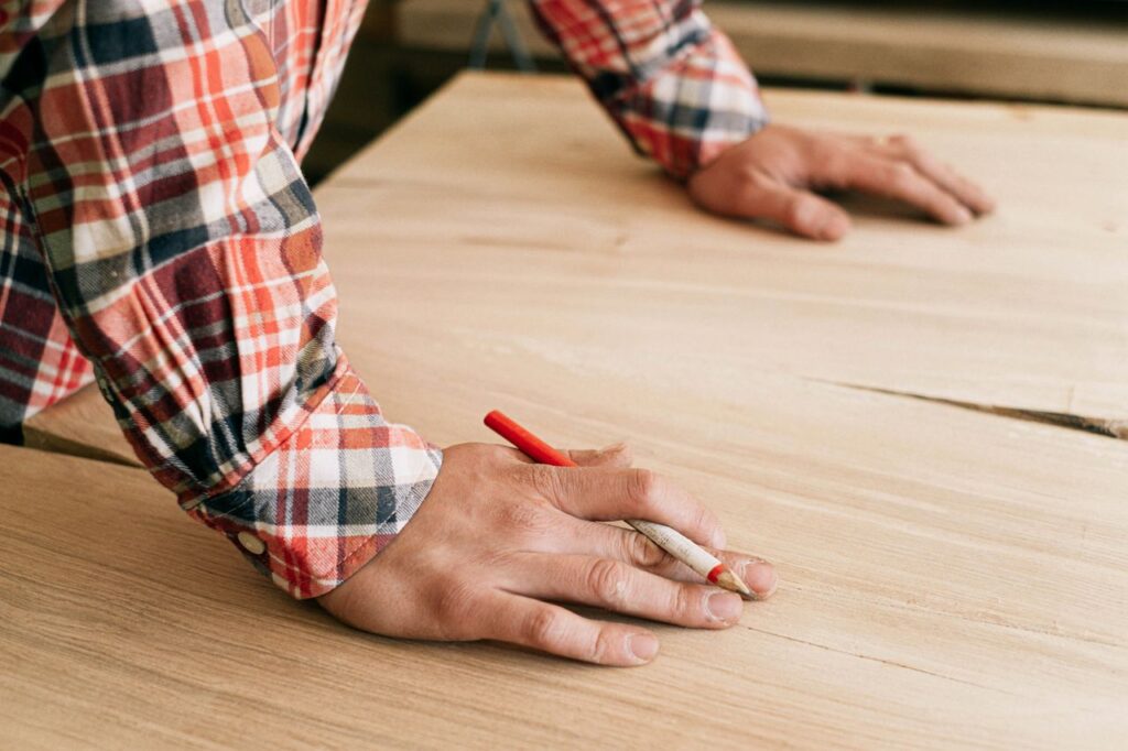 A craftsman marking wood in a workshop, focusing on precision and detail.