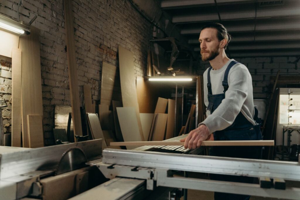 A focused male craftsman working with a saw in a woodworking workshop.